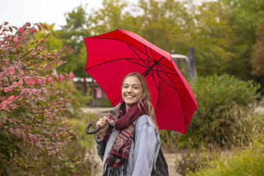 Glückliche Frau mit Regenschirm im Park - BFRF02342
