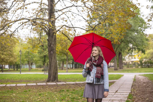 Junge Frau mit Regenschirm geht im Herbst im Park spazieren - BFRF02343