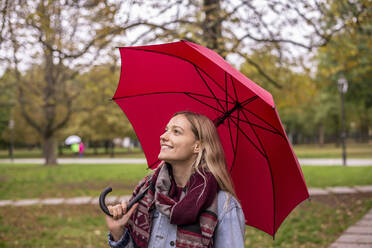 Thoughtful woman looking up with umbrella in autumnal park - BFRF02344