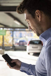 Male entrepreneur using smart phone in parking lot on sunny day - IFRF00197