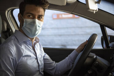 Männlicher Unternehmer mit Gesichtsschutzmaske, der während der Pandemie im Auto sitzt und wegschaut - IFRF00202