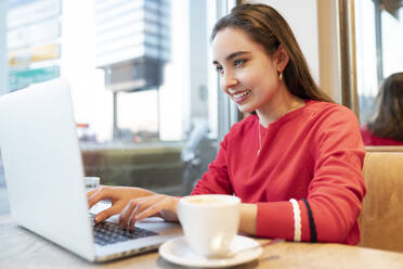 Lächelnde Frau, die einen Laptop benutzt, während sie in einem Café sitzt - JCCMF00239