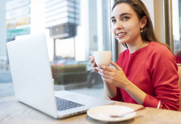 Schöne Frau mit Kaffeetasse und Laptop im Cafe sitzend - JCCMF00241