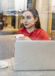 Junge Frau mit Kaffeetasse durch Glas im Café gesehen - JCCMF00245