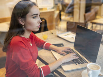 Nachdenkliche Frau mit Laptop durch das Glas eines Cafés gesehen - JCCMF00247