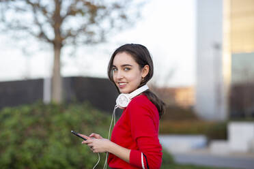 Junge Frau mit Kopfhörern und Smartphone im Park - JCCMF00249
