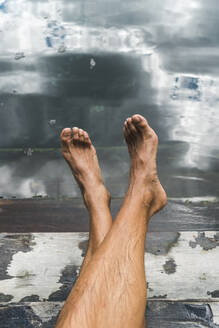 Bare feet of man relaxing on steps of underground cenote - JMPF00747