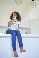 Lächelnde junge Frau mit Kaffeetasse auf dem Küchentisch zu Hause - KIJF03456