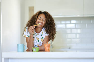 Lächelnde junge Frau isst Guacamole mit Karotten in der Küche - KIJF03458