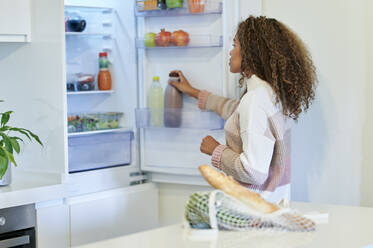 Junge Afro-Frau, die zu Hause Lebensmittel in den Kühlschrank stellt - KIJF03477