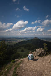 Female explorer admiring view of Burg Hohenzollern Castle while sitting on mountain at Swabian Alb, Germany - FDF00316