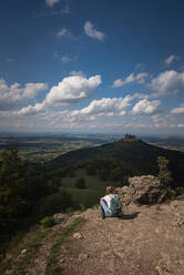 Weibliche Forscherin bewundert den Blick auf die Burg Hohenzollern, während sie auf einem Berg auf der Schwäbischen Alb sitzt, Deutschland - FDF00316