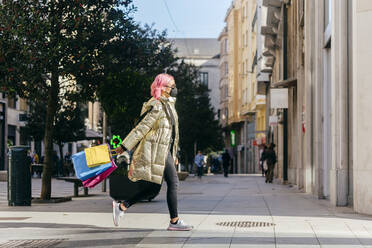 Frau mit Gesichtsmaske läuft mit Einkaufstüten auf dem Gehweg in der Stadt - MARF00044