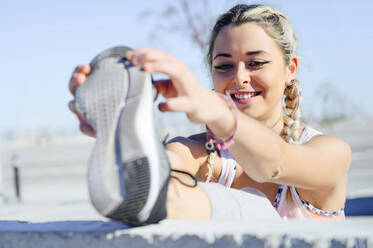 Lächelnde Sportlerin, die sich beim Training im Freien dehnt - PGF00302