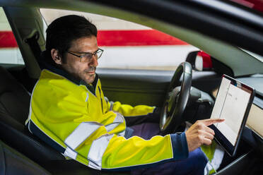 Männlicher Techniker in Uniform programmiert auf einem digitalen Tablet im Auto - DLTSF01427