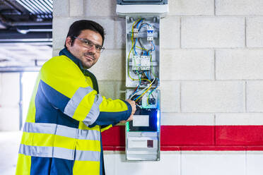 Lächelnder Techniker bei der Arbeit am Stromzähler in einer Autowerkstatt - DLTSF01451