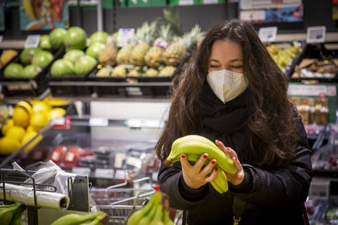 Ältere Frau kauft Bananen beim Lebensmitteleinkauf während COVID-19 - NGF00733