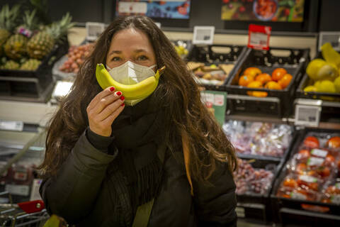 Mature woman in protective face mask showing banana while shopping in supermarket stock photo
