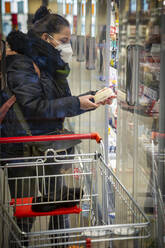 Ältere Frau mit Einkaufswagen beim Einkaufen im Supermarkt während COVID-19 - NGF00736
