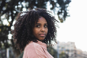 Confident young woman with curly hair looking away in city - PNAF00324