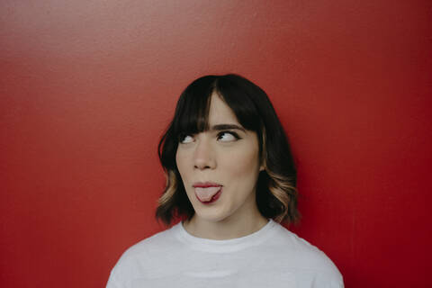 Young woman sticking out tongue while looking up against red background stock photo