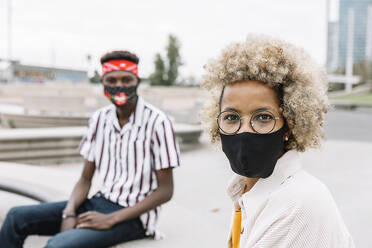 Man and woman wearing face mask staring while sitting on bench - XLGF00908