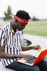 Mid adult man with credit card doing shopping on laptop while sitting outdoors - XLGF00918