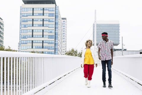 Mid adult woman and man talking while walking on bridge in city stock photo
