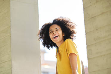 Curly hair student laughing while standing at university - AODF00013