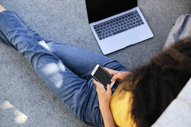 Universitätsstudent mit Laptop und Mobiltelefon auf dem Gehweg sitzend - AODF00017