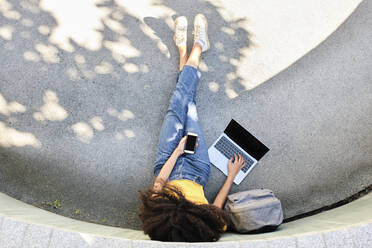 Student mit Mobiltelefon und Laptop auf dem Gehweg sitzend - AODF00018
