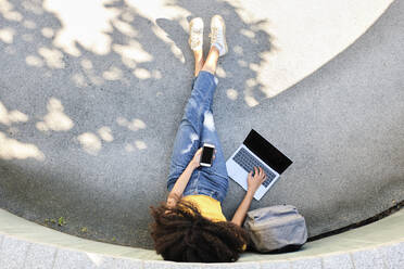 Student with mobile phone using laptop while sitting on footpath - AODF00018