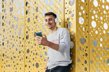 Smiling man listening music while leaning on wall - MARF00057