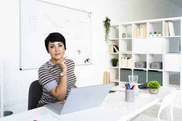 Portrait of businesswoman working at office in front of laptop - GIOF10095