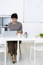 Porträt einer Geschäftsfrau, die am Bürotisch sitzt und ihr Smartphone in der Hand hält - GIOF10105
