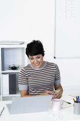 Portrait of businesswoman sitting at office desk with smart phone in hands - GIOF10106