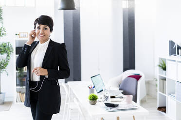 Portrait of businesswoman smiling while using smart phone with headphones - GIOF10126