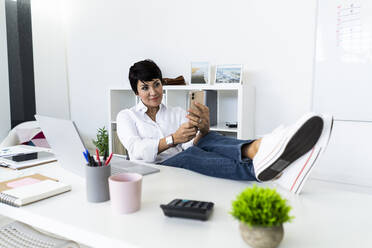 Portrait of businesswoman taking break with smart phone at office table - GIOF10155