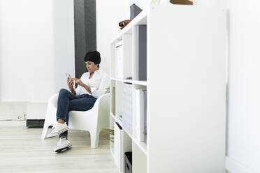 Businesswoman sitting in office armchair with smart phone in hands - GIOF10162