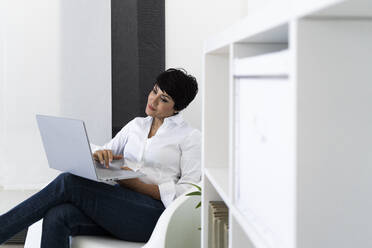 Geschäftsfrau in Bürosessel mit Laptop sitzend - GIOF10166