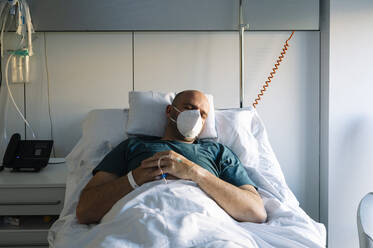 Patient mit Gesichtsschutzmaske schläft auf einem Bett im Krankenhaus - JCMF01676