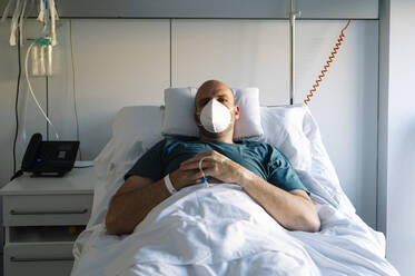 Patient mit Gesichtsschutzmaske auf dem Bett im Krankenhaus liegend - JCMF01677