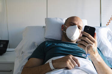 Ein Patient benutzt ein Mobiltelefon, während er im Krankenhaus im Bett liegt - JCMF01678