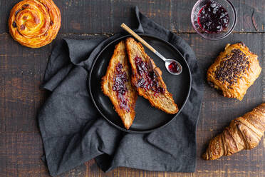 Draufsicht auf leckere hausgemachte Croissants mit süßer Kirschmarmelade auf einem Holztisch mit leckeren Brötchen mit Schokolade und Rosinenbrötchen - ADSF19235