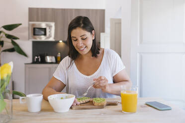 Smiley woman preparing healthy breakfast with avocado toasts and orange juice - ADSF19239