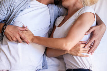 From above cropped unrecognizable couple in casual wear lying on soft bed at home and delicately cuddling - ADSF19313