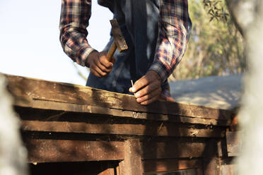 Young man hammering nail on wood during sunny day - JPTF00617