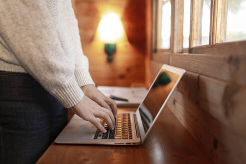 Junger Mann mit Laptop auf Holztisch in Blockhütte - JPTF00624