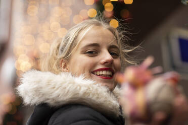 Glückliche junge Frau mit Dekoration gegen Weihnachtsbeleuchtung - SGF02725