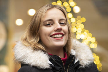 Bond young woman smiling against Christmas lights during holidays - SGF02728